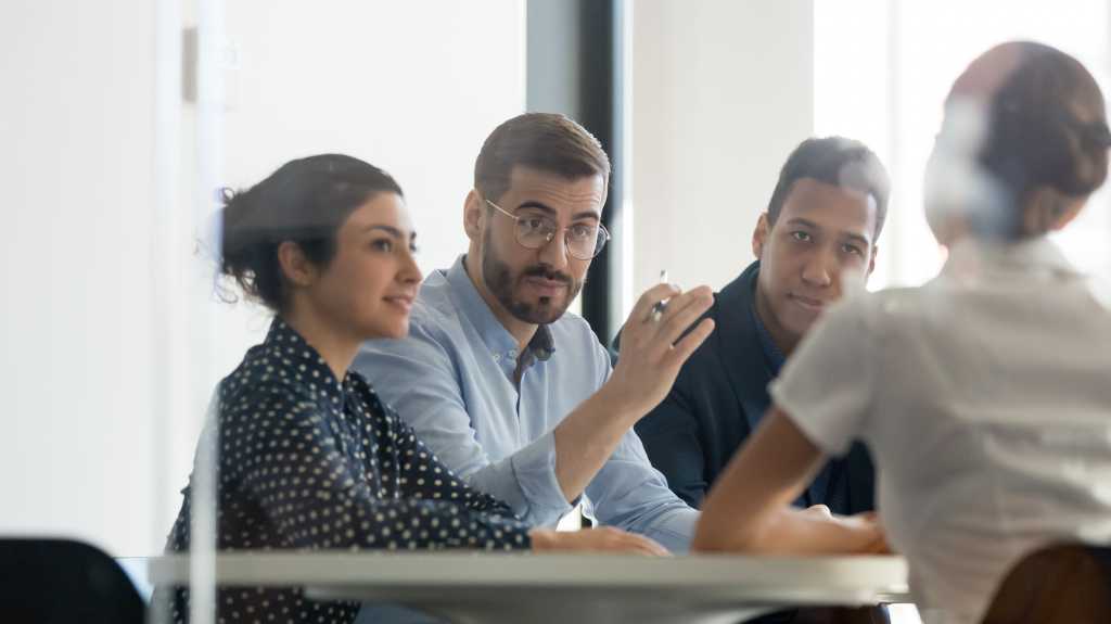 Serious male boss team leader hr recruiter talking to businesswoman client applicant at job interview or corporate briefing sit at table, businessman executive negotiating at diverse group meeting