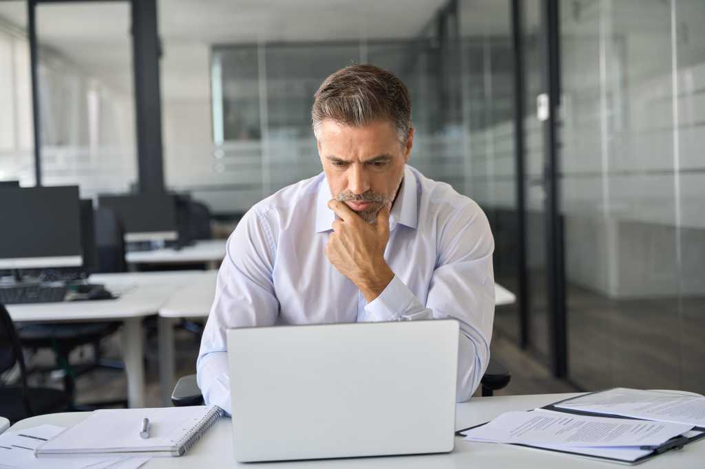 Serious busy mature professional business man company ceo executive manager investor looking at laptop pc computer sitting in office thinking of corporate management plan and financial strategy risks.