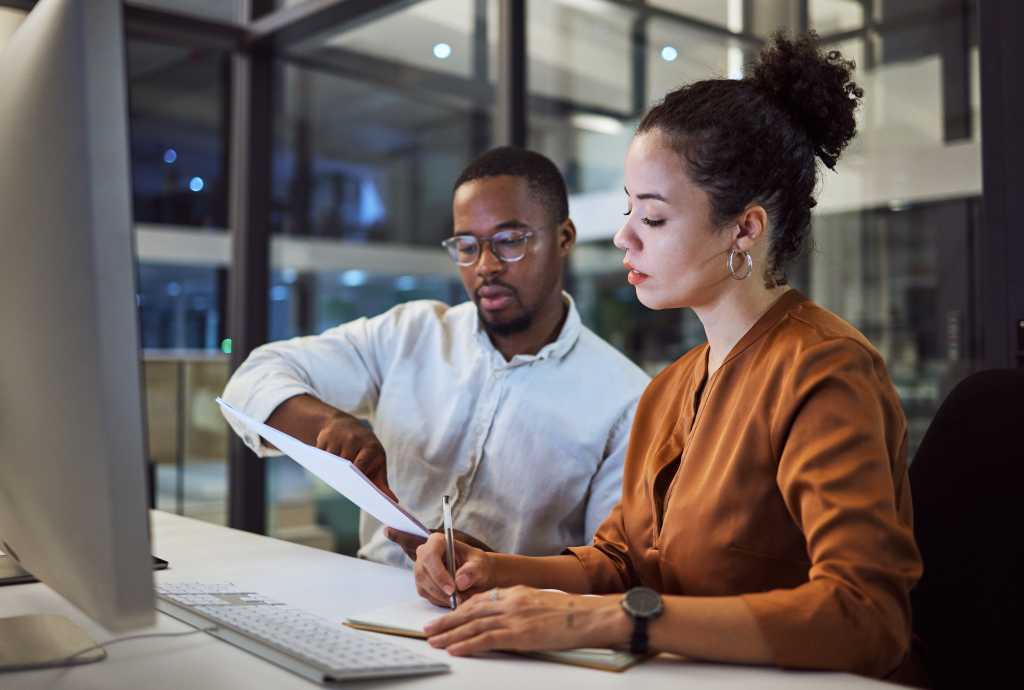 Teamwork in New York office at night, business document reading together and professional accounting report. Black man with financial audit, showing latino woman figures and employee collaboration