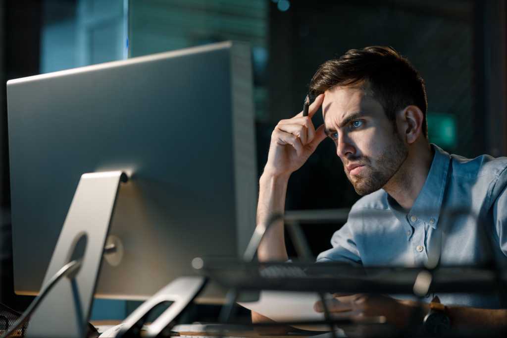 Man focusing on information in computer working alone late at night in modern office.