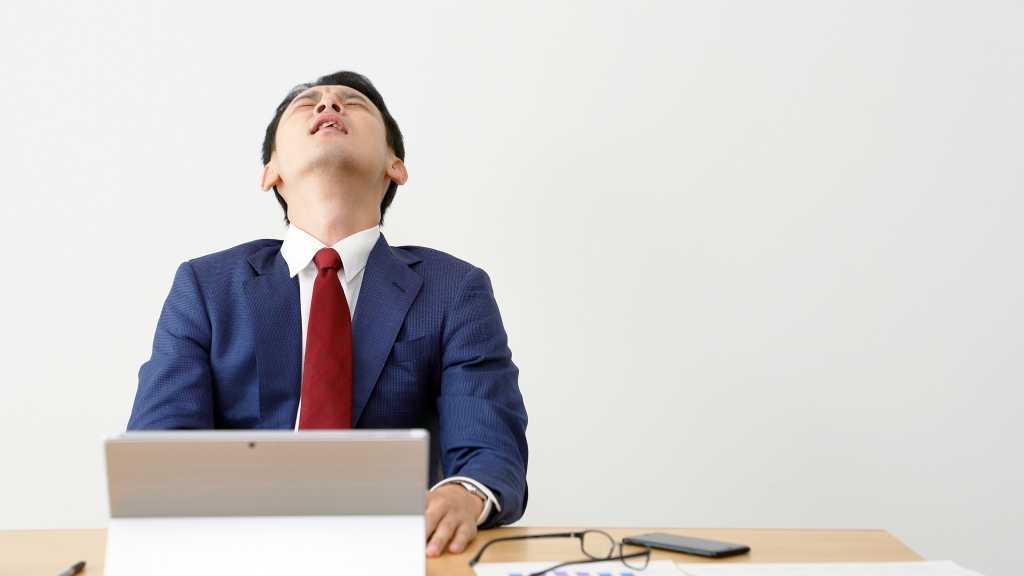 frustrated businessman at laptop throwing head back in despair