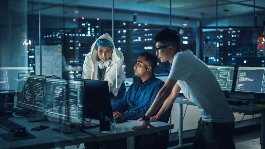 Diverse Team of Professionals Meeting in Office at Night: Brainstorming IT Programmers Use Computer Together, Talk Strategy, Discuss Planning. Software Engineers Develop Inspirational App Program