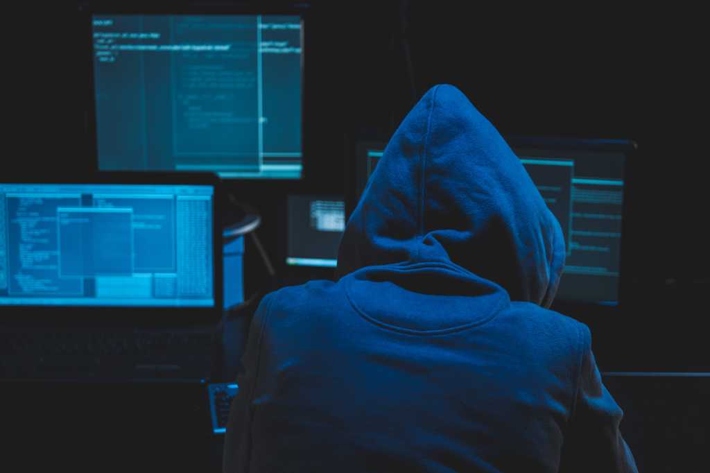 Hacker using computer for organizing massive data breach attack on goverment servers. Hacker in dark room surrounded computers